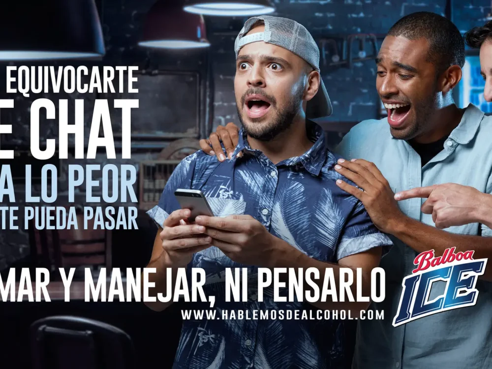 Tres amigos en un bar, uno tiene cara de preocupado mientras sostiene su celular, los otros dos amigos se burlan de él. Texto dice: Que equivocarte de chat sea lo peor que te pueda pasar. Tomar y manejar ni pensarlo.