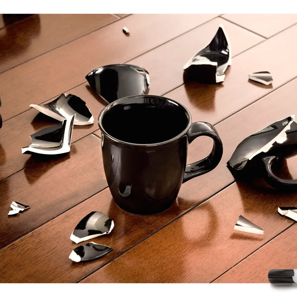 Una taza intacta en el suelo, a su alrededor hay trozos de otra taza rota. Abajo se ve el logo de un pegamento.